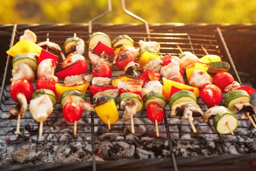 Tasty chicken and vegetable shashlik roasting on on skewers over hot grill in countryside