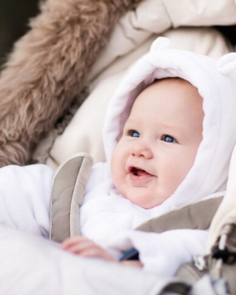 Happy laughing baby enjoying a walk in winter park sitting in a warm stroller with sheepskin hood